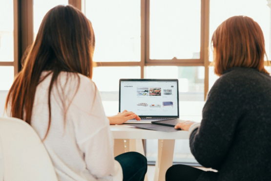 two-women-talking-while-looking-at-laptop-computer.jpg two women talking while looking at laptop computer